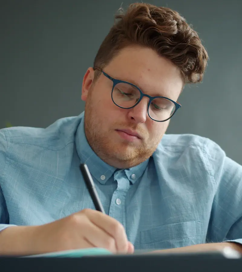 A young man studying with glasses, writing in a notebook